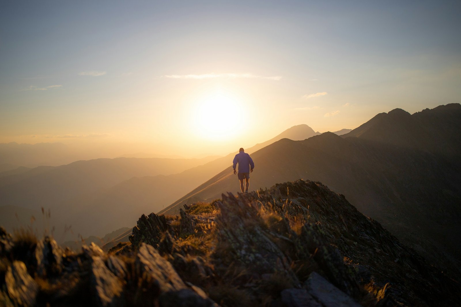 A lone figure standing on a mountain ridge, facing the sunrise on the horizon